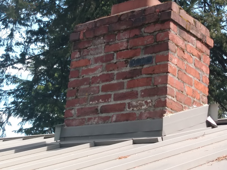 Linear chimney flashing installed in a chimney surrounded by a metal roof.